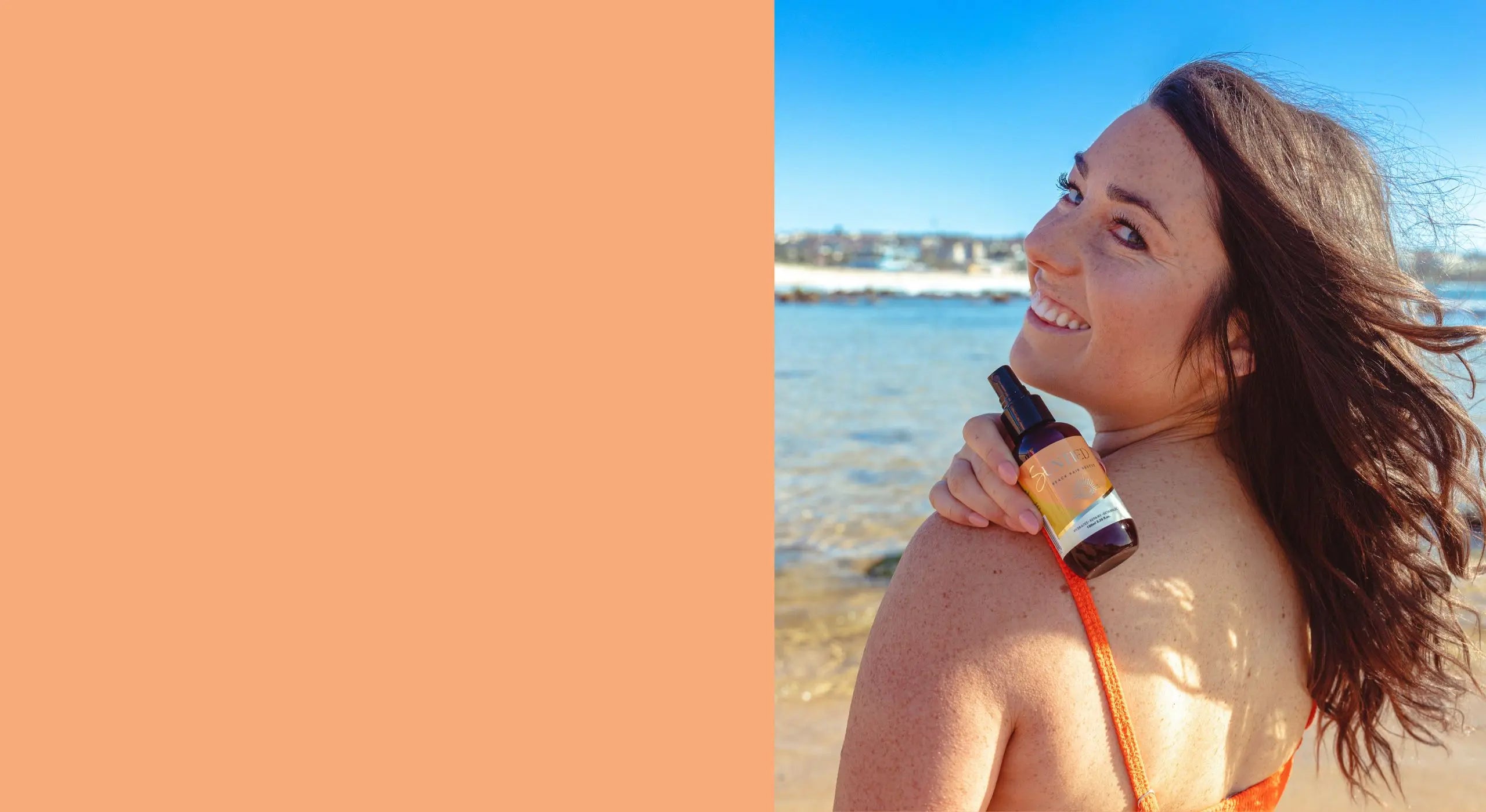 Woman with long wavy hair smiling at the beach, holding Suntied Leave-In Conditioner Spray, promoting low-maintenance hairstyles and UV hair protection in Australia.